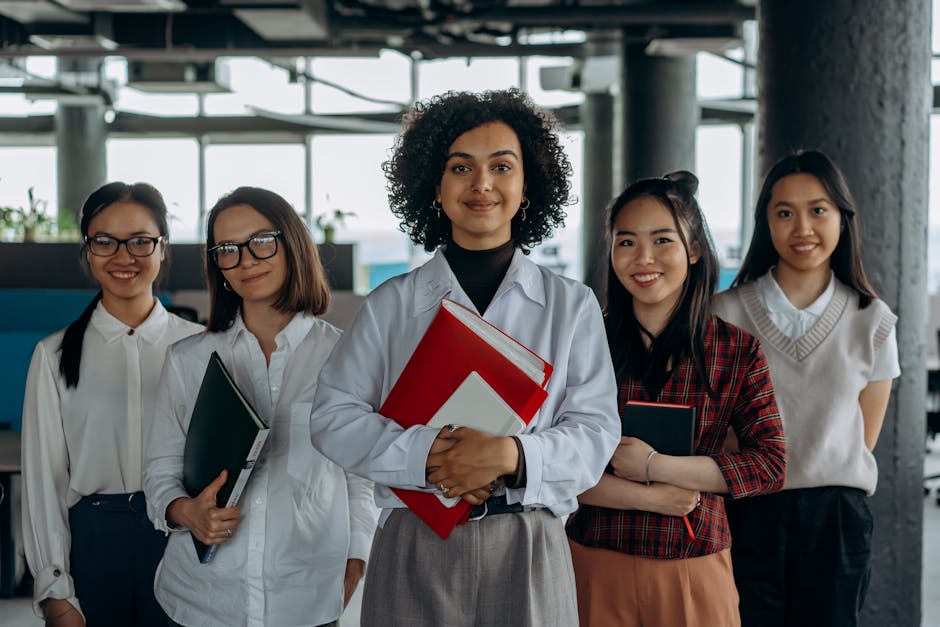 Group of diverse women colleagues smiling in a modern office setting, holding documents